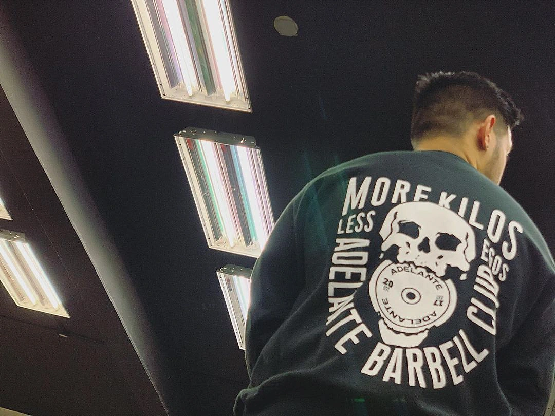 Skull illustration with typographic badge-like layout of Adelante Barbell Club's "More Kilos Less Egos" merch line, back view
